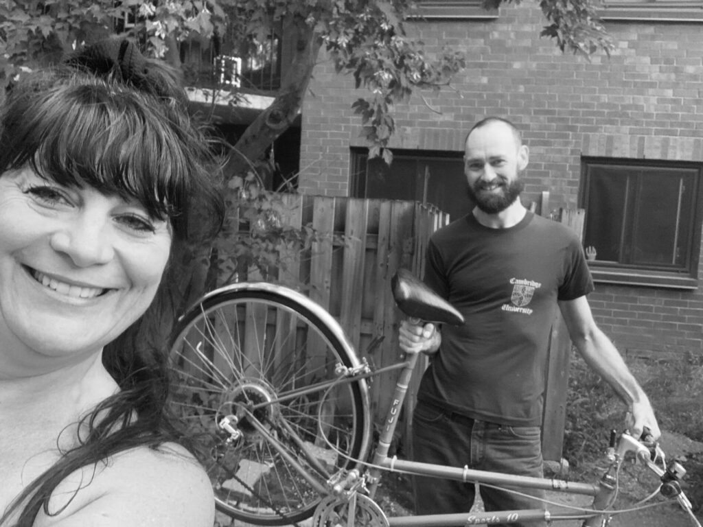A selfie of two people smiling. The person not taking the selfie is holding an adult bicycle.